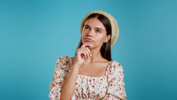 Retrato de una joven pensando en una mujer con sombrero que tiene un momento de idea apuntando con el dedo hacia arriba en el fondo azul del estudio. Sonriente chica feliz mostrando gesto eureka. — Vídeo de stock