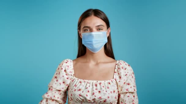 Donna attraente in respiratore protettivo mostrando Ok segno su sfondo blu. Ragazza positiva in maschera sorride alla telecamera durante la quarantena. Vincitore. Successo. Linguaggio del corpo. — Video Stock