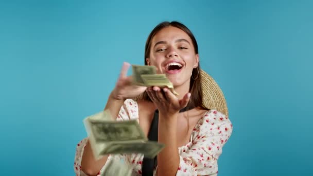 Красуня з здивованим щасливим обличчям розсіює, марнує гроші. Дівчинка перевитрачає американську валюту. Леді переповнена доларами на синьому студійному фоні. . — стокове відео