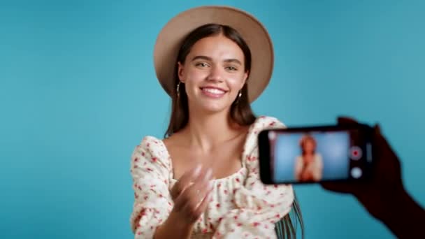 Senyum vlogger wanita merekam video dirinya menari di depan kamera smartphone di latar belakang biru. Pengaruh membuat klip media sosial yang lucu — Stok Video