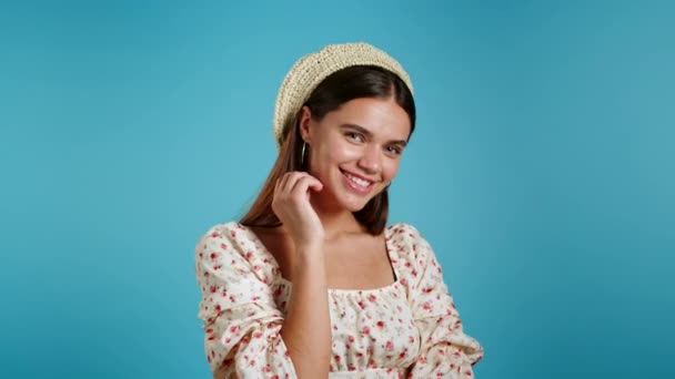 Mooi jong meisje met lang haar op een blauwe studio achtergrond, lachend en flirtend. Schattig portret van vrouw in bloemenjurk. — Stockvideo