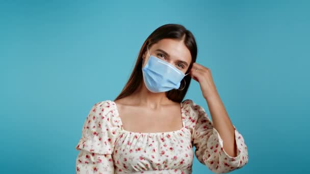 Tevreden vrouw in jurk verwijderd beschermende masker en gooit het op de vloer als symbool van pandemie, epidemie einde. Blauwe studio achtergrond. — Stockvideo