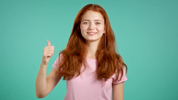 Młoda kobieta pokazuje kciuk na niebieskim tle. Pozytywna młoda dziewczyna uśmiecha się do kamery. Zwycięzca. Sukces. Język ciała. — Wideo stockowe