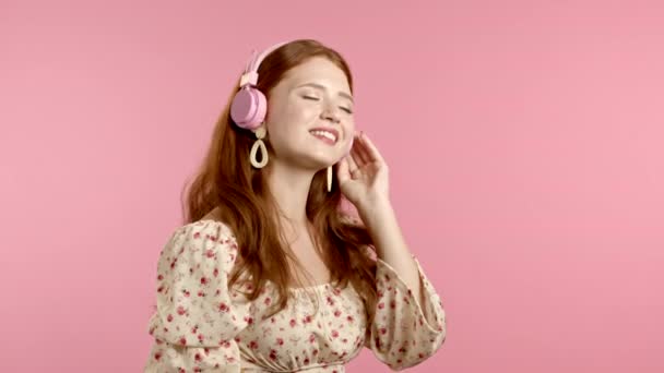 Όμορφη νεαρή κοπέλα με κόκκινα μαλλιά διασκεδάζει, χαμογελά, χορεύει με ροζ ακουστικά στο στούντιο. Μουσική, χορός, ραδιοφωνική ιδέα, αργή κίνηση — Αρχείο Βίντεο