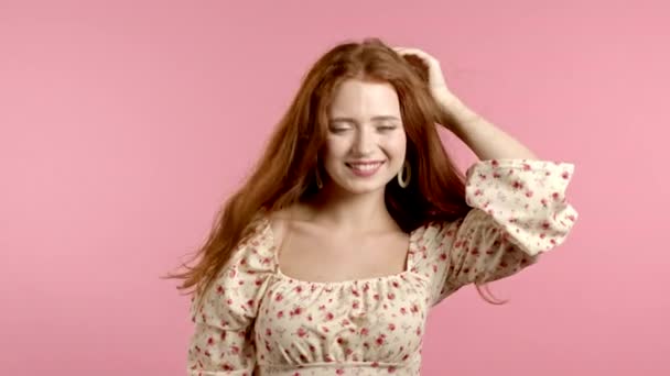 Mujer joven en vestido floral mirando a la cámara, coqueteando. Retrato de hermosa chica en fondo de estudio de pared rosa. — Vídeos de Stock