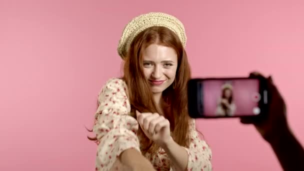 Улыбающаяся блогер записывает видео, где она танцует перед камерой смартфона на розовом фоне. Влиятель делает смешной клип в социальных сетях — стоковое видео
