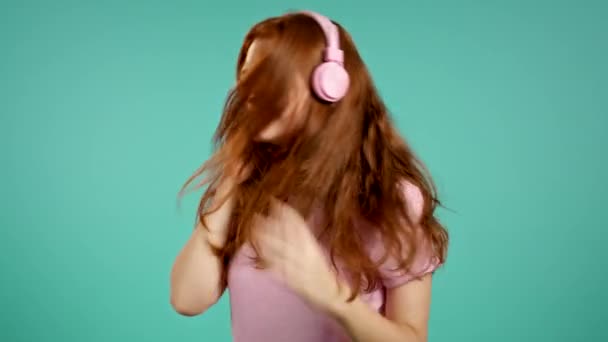 Jolie jeune fille aux cheveux longs écoutant de la musique, souriant, dansant dans des écouteurs en studio sur fond bleu. Musique, danse, concept radio, ralenti — Video
