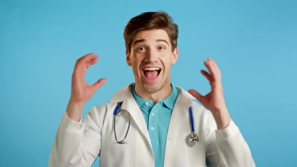 Удивительный доктор шокирован, говоря: "Ух ты!" Красивый доктор в медицинском пальто, удивленный на голубом фоне. — стоковое видео