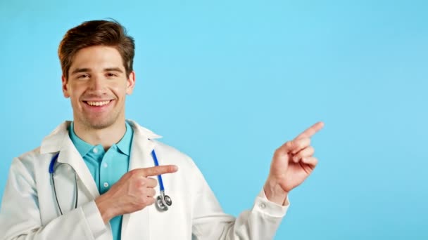 Portrait de l'espace de copie de l'homme souriant en manteau médical professionnel blanc indique avec les mains sur son côté gauche vers le haut. Docteur présentant et montrant quelque chose d'isolé sur fond bleu. — Video