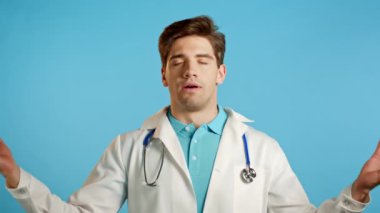 Beyaz önlüklü sakin doktor dinleniyor, meditasyon yapıyor. Adam sakinleşir, derin derin nefes alır mavi stüdyo arka planında Mudra om.