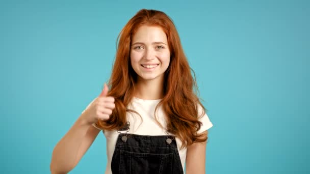 Leuke vrouw met duim omhoog teken over blauwe achtergrond. Positief jong meisje lacht naar de camera. Winnaar. Succes. Lichaamstaal. — Stockvideo