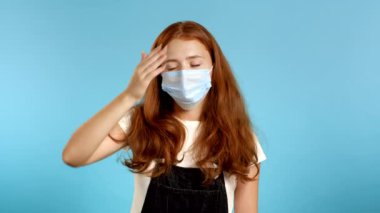 Koruyucu maskeli genç bir kadının portresi facepalm hareketi yapıyor, hayır, unuttum. Uzun saçlı mutsuz bir kadın. Üzüntü, pişmanlık, drama, başarısızlık. Mavi duvarda izole edilmiş.