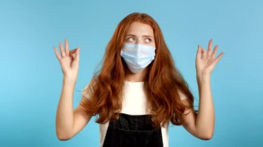 Koruyucu maskeli sakin kız dinleniyor, meditasyon yapıyor. Kadın sakinleşir, derin derin nefes alır. Mavi stüdyo arka planında Mudra om. Yoga konsepti.