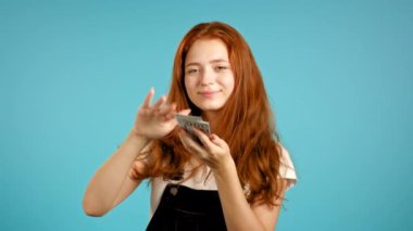 Mutlu yüzü olan güzel bir kadın, boşa para harcıyor. Kız Amerikan dolarını fazla harcadı. Hanımefendinin mavi stüdyo arka planında dolarlar var. .