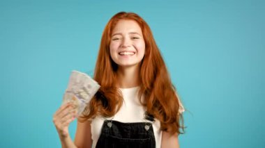 Şaşırtıcı derecede mutlu, heyecanlı bir kadın mavi duvarda Amerikan doları banknotları gösteriyor. Başarı, kazanç, zafer sembolü.