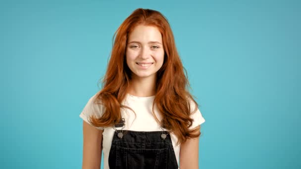 Jeune femme avec une coiffure rouge dans l'ensemble regardant à la caméra. Portrait de mignonne belle fille sur fond de studio mur bleu. — Video