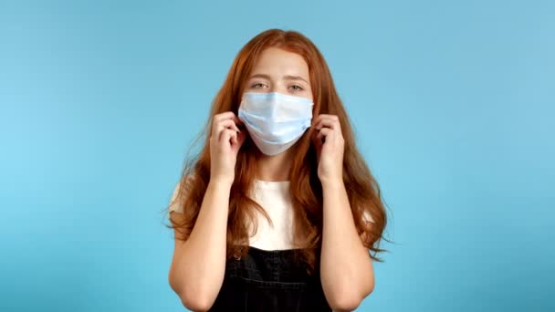 Pleased woman in overall removed protective mask and throws it on floor as symbol of pandemic, epidemic end. Blue studio background. — Stock Video