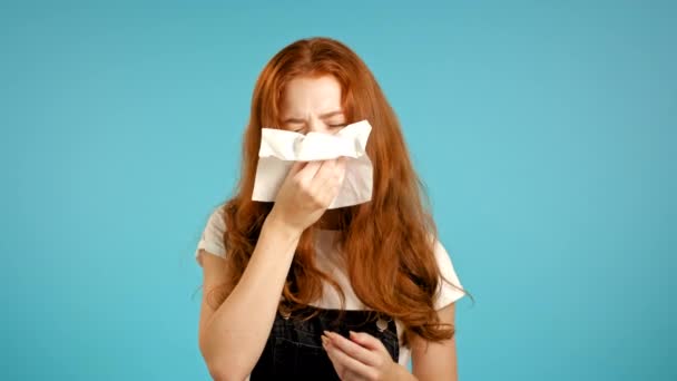 Rapariga muito doente espirra para o tecido. Mulher isolada no fundo do estúdio azul. Ela está doente, tem uma reação fria ou alérgica. Coronavírus, epidemia 2020, doença conceito. — Vídeo de Stock