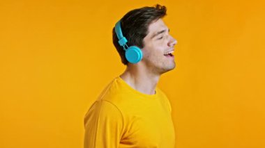 Moda saçı olan yakışıklı genç adam. Stüdyoda sarı arka planda mavi kulaklıklarla dans ediyor, gülüyor. Müzik, dans, radyo konsepti, yavaş çekim