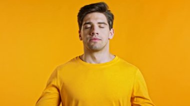 Sakin adam dinleniyor, meditasyon yapıyor. Sakinleşir, sarı stüdyo arka planında derin derin nefes alır. Yoga konsepti.