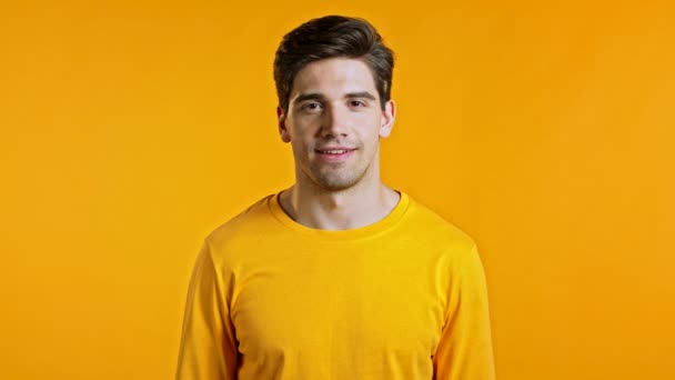 Retrato de homem bonito em amarelo t-shirt piscando com o olho, flertando e sorrindo para a câmera. Cara em estúdio em fundo brilhante. — Vídeo de Stock