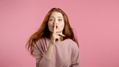 Güzel bir kadın parmaklarını pembe arka planda tutuyor. Şşş, sır, sessizlik jesti. Kapat..