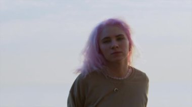 Pembe saçlı, dans eden genç kız. Acayip hip-hop hareketleri. Modern kadın gökyüzü arka planında serbest dans gösterisi yapıyor. Yavaş çekim.