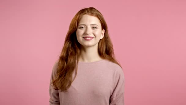 Giovane donna sorridente con acconciatura rossa in cerca di fotocamera. Ritratto di bella ragazza carina su sfondo rosa studio parete. — Video Stock