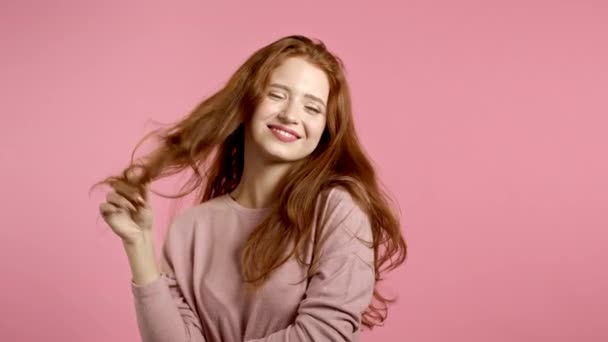 Портрет флирта красивой девушки на фоне розовой стены студии. Молодая женщина смотрит в камеру, игриво вертит волосами вокруг пальца — стоковое видео
