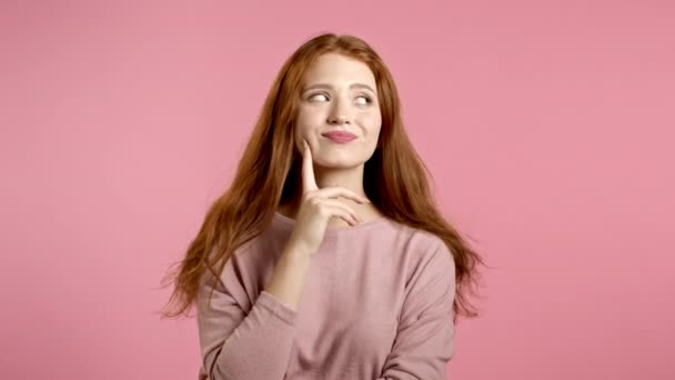 Denkende vrouw op en neer kijkend op een roze achtergrond. Gelukkige glimlachende gezichtsuitdrukkingen. Mooi model met aantrekkelijk uiterlijk. — Stockvideo