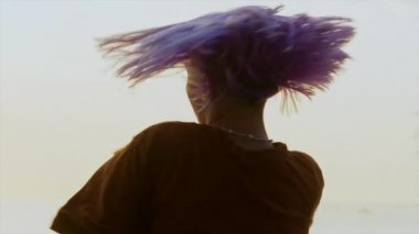 Menekşe boyalı saçlı, dans eden yetenekli ucube kadının portresi. Serbest stil hip-hop hareketleri yapan bir kız. Gün batımında okyanus ya da deniz kenarında açık hava eğitimi.