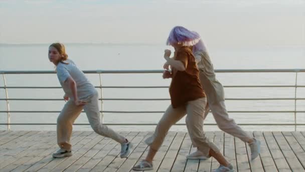 Tańcząca grupa młodych utalentowanych dziwolągów wykonujących ruchy hip-hopowe. Dziewczyny cieszą się nowoczesną ekspresją tańca. Trening na świeżym powietrzu w pobliżu morza lub oceanu podczas zachodu słońca. — Wideo stockowe