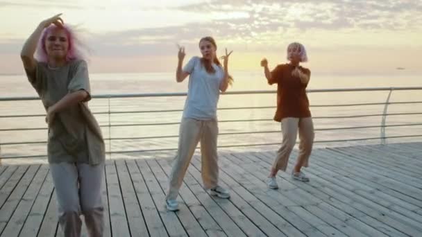 Junge tanzende Teenie-Mädchen genießen flippige Hip-Hop-Bewegungen. Moderne Frauen tanzen bei Sonnenaufgang gemeinsam Freestyle auf dem Meeresufer. Zeitlupe. — Stockvideo