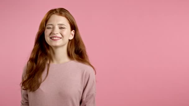 Ricevuto. Giovane donna sorridente con acconciatura rossa in cerca di fotocamera. Ritratto di bella ragazza carina su sfondo rosa studio parete. — Video Stock