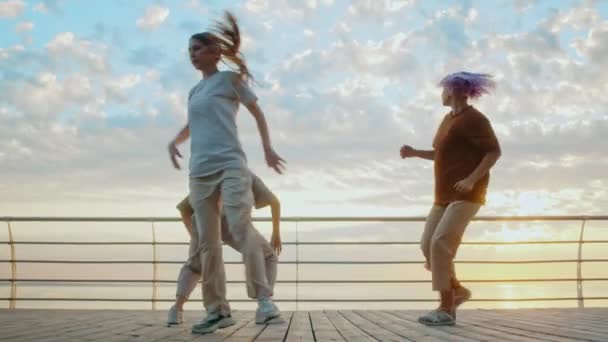 Junge kreative Tänzerinnen und Tänzer genießen flippige Hip-Hop-Moves. Moderne Frauen tanzen bei Sonnenaufgang gemeinsam Freestyle auf dem Meeresufer. Zeitlupe. — Stockvideo