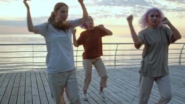 Dans eden genç kızlar hip-hop hareketlerinden hoşlanıyorlar. Modern kadınlar gün doğumunda deniz setinde serbest dans ediyorlar. Yavaş çekim. — Stok video