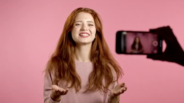 Smiling blogger woman making online new video blog, vlog, with her smartphone on pink background. Influencer speaking to camera during conference call record. — Stock Video