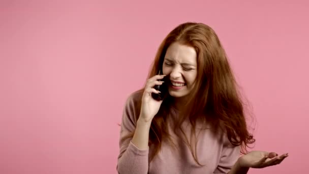 Chica bonita con el pelo largo habla por teléfono y se ríe infecciosamente de los chistes de los interlocutores. Traje de moda. Fondo de estudio rosa — Vídeos de Stock