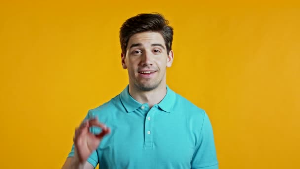 Hezký mladý muž v modrých úsměvech před kamerou. Chlápek ukazující na žlutém pozadí značku OK. Vítěz. Úspěch. Jazyk těla. — Stock video