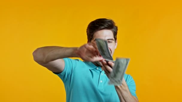 Man with surprised happy face scatters, waste money. Person overspend US currency. Guy in blue is flush with dollars on yellow studio background . — Stock Video