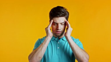 Baş ağrısı çeken genç bir adam, stüdyo portresi. Adam ellerini başının üstüne koyuyor, sarı arka planda izole edilmiş. Sorunlar, ilaç, hastalık kavramı