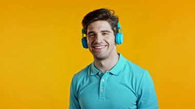 Moda saçı olan yakışıklı genç adam. Stüdyoda sarı arka planda mavi kulaklıklarla eğleniyor, gülümsüyor, dans ediyor. Müzik, dans, radyo konsepti, yavaş çekim