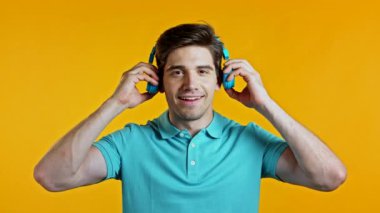 Mavi kulaklık takan yakışıklı genç adam, gülümsüyor, sarı arka planda dans ediyor. Müzik, dans, radyo konsepti, yavaş çekim