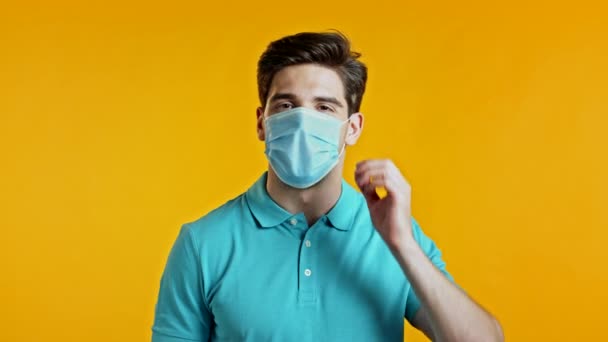 Удовлетворенный мужчина в синей короткой защитной маске снимает ее и бросает на пол как символ пандемии, эпидемии конца. Желтый фон студии. — стоковое видео
