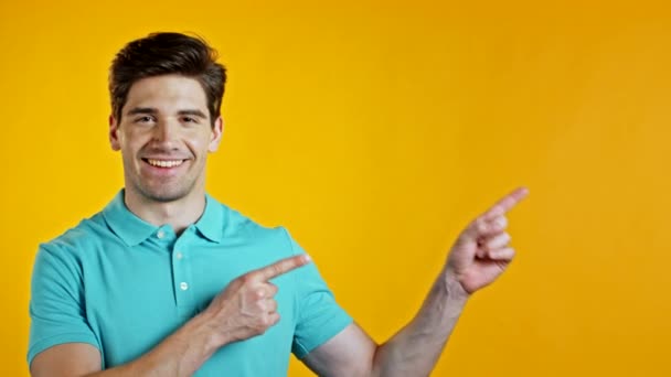 Portrait de l'espace de copie de l'homme souriant en bleu indique avec les mains sur le côté gauche vers le haut. Le gars qui présente et montre quelque chose d'isolé sur fond jaune. — Video