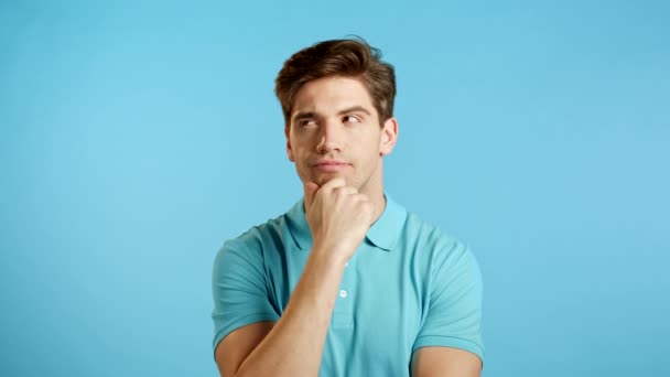 Portrét mladého přemýšlejícího muže, který má myšlenkový moment ukazující prstem na pozadí modrého studia. Usmívající se šťastný student chlap ukazující eureka gesto. — Stock video