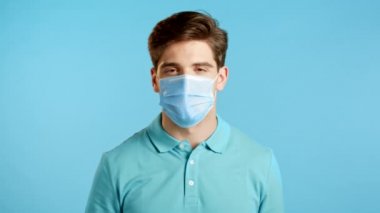 Koruyucu tıbbi maske takan yakışıklı bir genç. Stüdyonun arka planını imzalamak gibi. Kazandım. Başarı. Vücut dili.