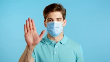 Koruyucu maskeli bir adam el işareti olmadan onaylamıyor. Reddetmek, reddetmek, katılmamak, mavi arka planda erkek ya da öğrencinin portresi