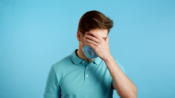 Hombre europeo frustrado en máscara protectora haciendo gesto de la palma de la cara sobre fondo azul de la pared. El tipo está cansado, aburrido de la epidemia, covid, decepcionado, indefenso — Vídeos de Stock