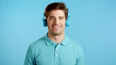 Moda saçı olan yakışıklı genç adam stüdyoda eğlenceli, gülümseyen, mavi kulaklıklarla dans eden. Müzik, dans, radyo konsepti, yavaş çekim